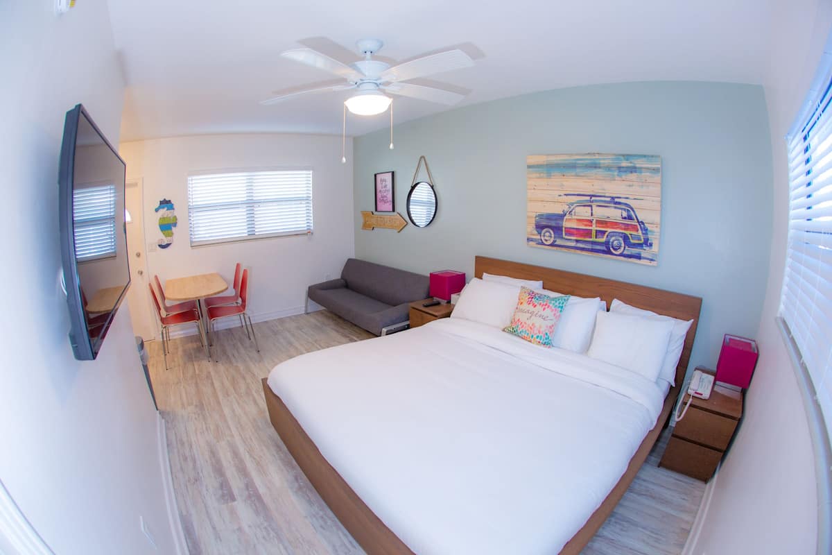 Une chambre d’hôtel avec un lit, un bureau, une chaise, un canapé, un ventilateur de plafond et un tableau au mur.