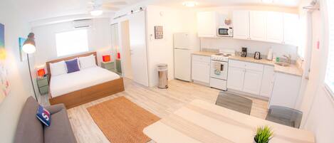 A compact hotel room with a bed, a small sofa, a kitchenette, and a dining area.
