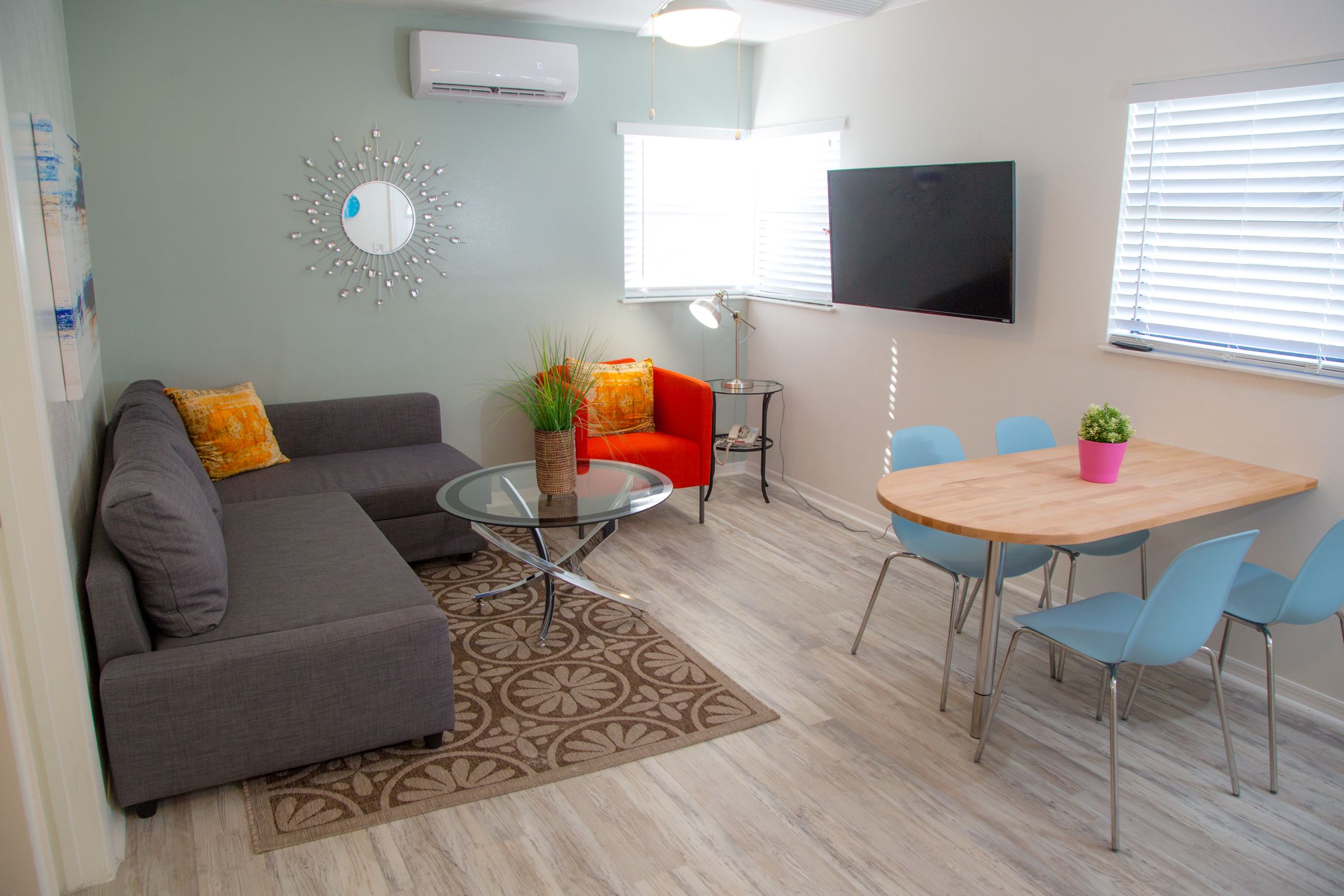 A living room with a grey sectional sofa, a red armchair, a glass coffee table, and a wooden dining table with four chairs.