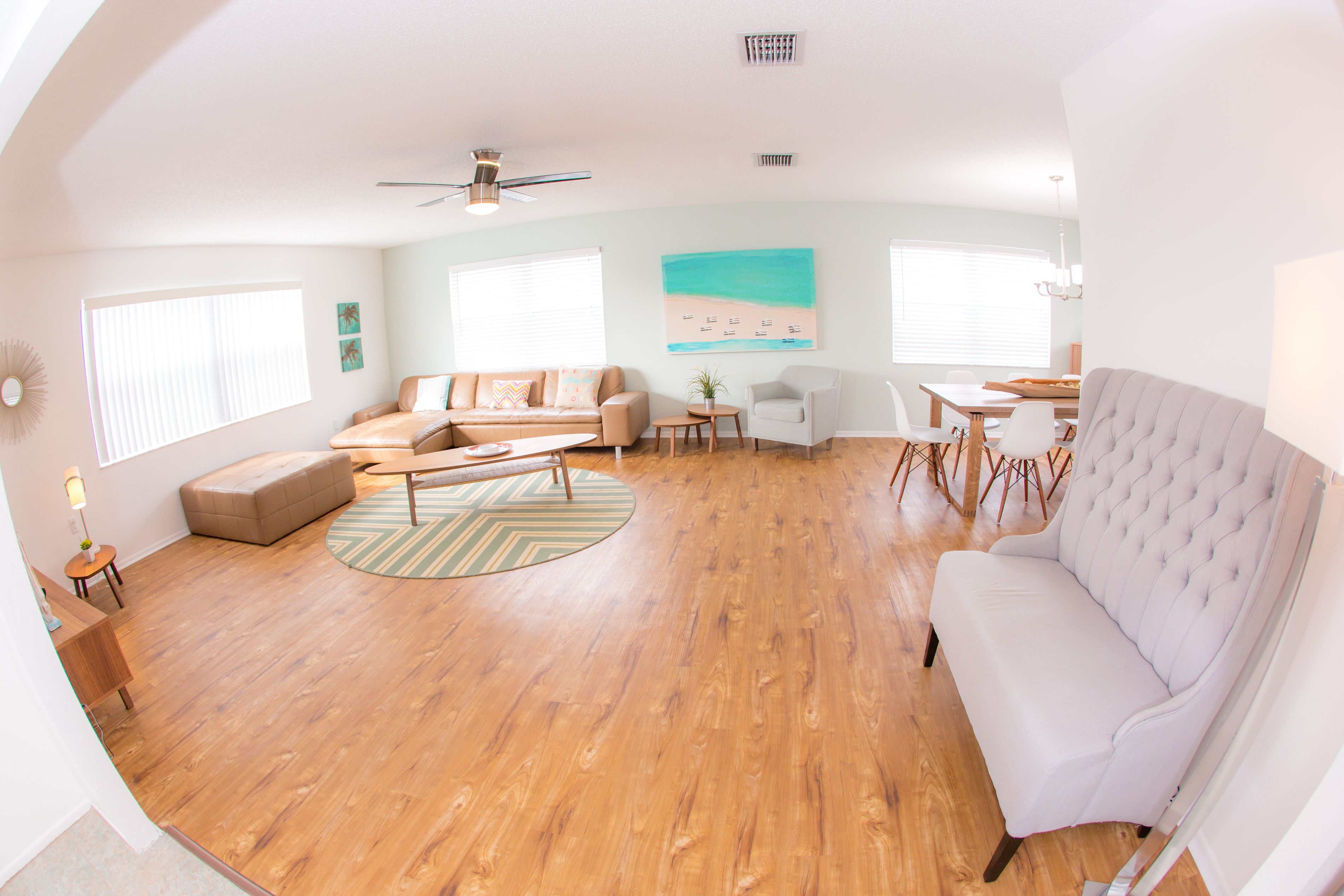 A spacious living room with a wooden floor, a white sofa, a beige sofa, a round coffee table, and a dining area with a wooden table and chairs.