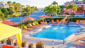 A swimming pool with lounge chairs and umbrellas, surrounded by palm trees and a white fence. - St Pete Beach Suites (St. Pete Beach)