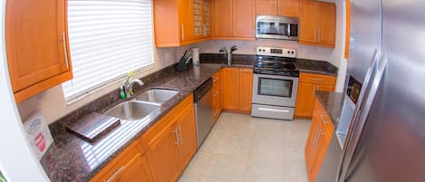 A compact kitchen with wooden cabinets, a stainless steel refrigerator, a microwave, an oven, and a granite countertop.