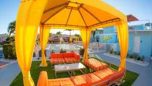 An outdoor seating area with orange and white striped cushions, a white table, and a yellow canopy. - St Pete Beach Suites (St. Pete Beach)