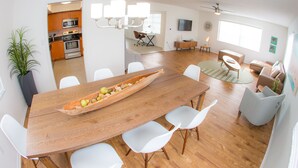 A spacious living area with a wooden dining table, white chairs, a kitchen with wooden cabinets, a ceiling fan, and a large window providing natural light. - St Pete Beach Suites (St. Pete Beach)
