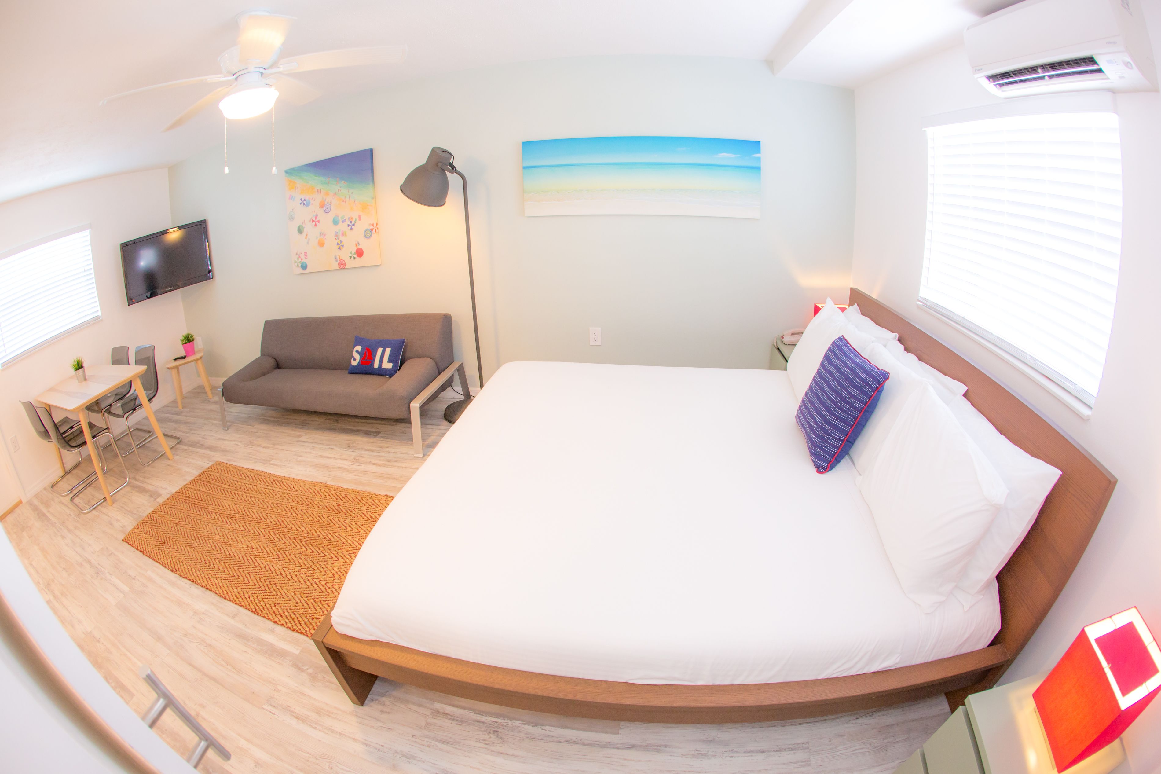 Ein Schlafzimmer mit einem großen Bett, einem Schreibtisch, einer Couch, einem Fernseher und Kunstwerken an den Wänden.
