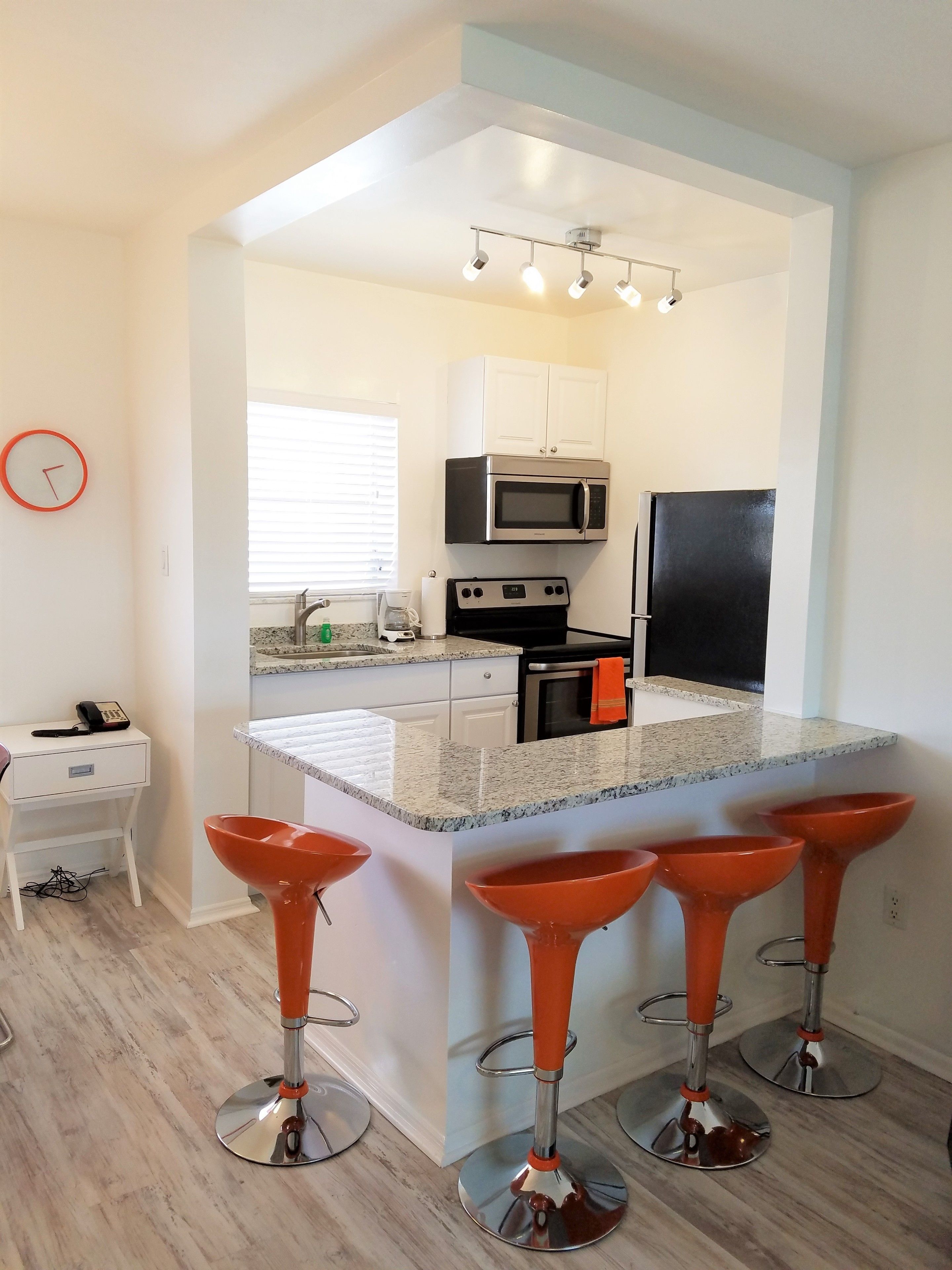 A modern kitchen with a central island, stainless steel appliances, and a clock on the wall.