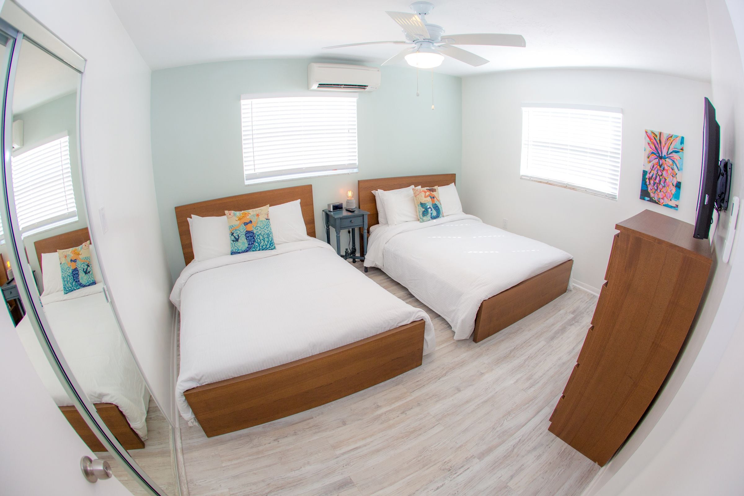 A bedroom with two beds, a ceiling fan, and a TV.