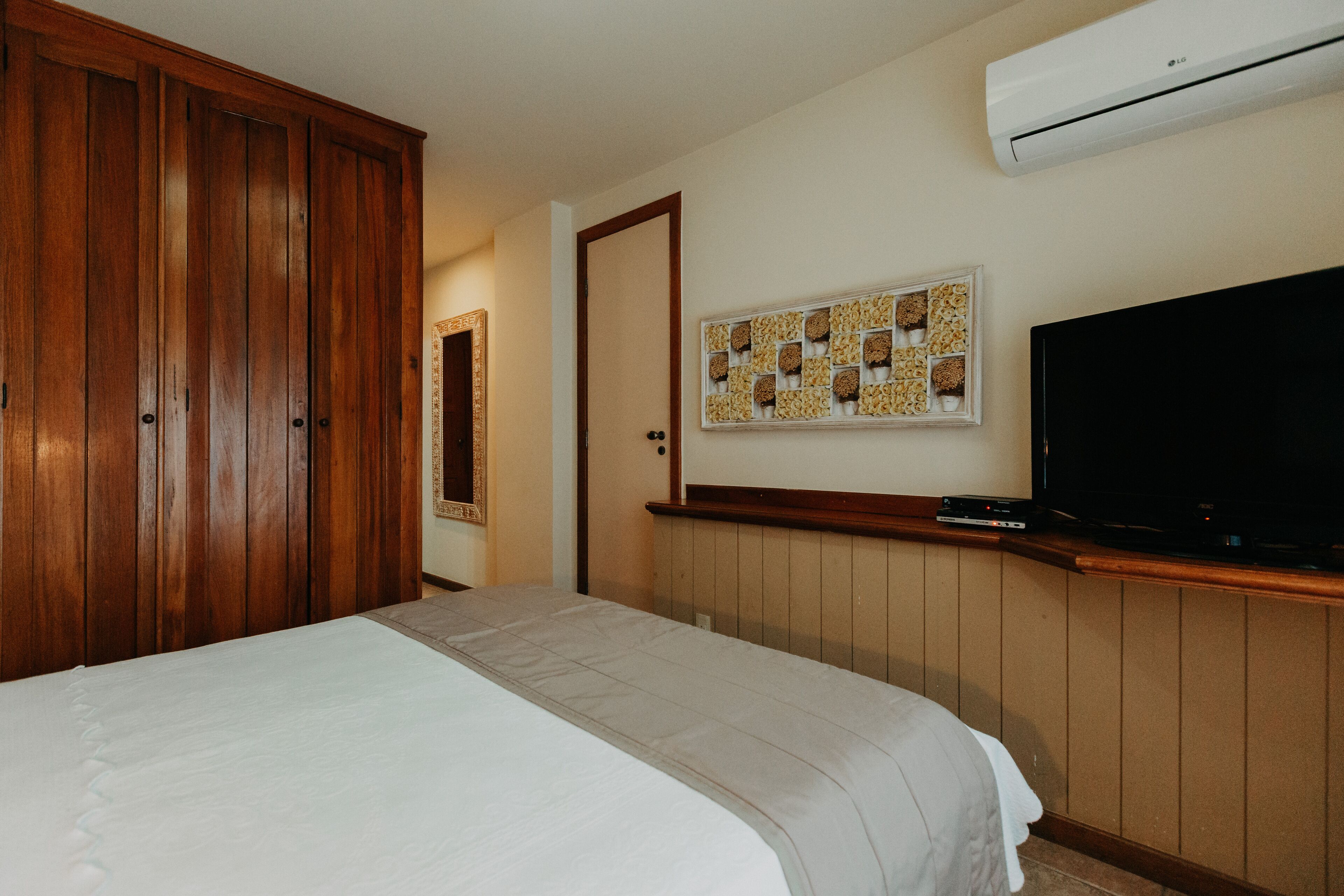 Een hotelkamer met een groot bed, een houten garderobe, een flatscreen televisie en een airconditioning.