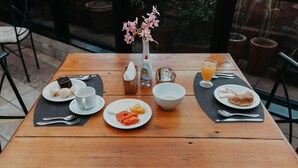 A wooden table with a breakfast setting including plates of food, a vase with flowers, a bottle, and a glass of orange juice. - Kastel Itaipava Centro Hotel (Petrópolis)