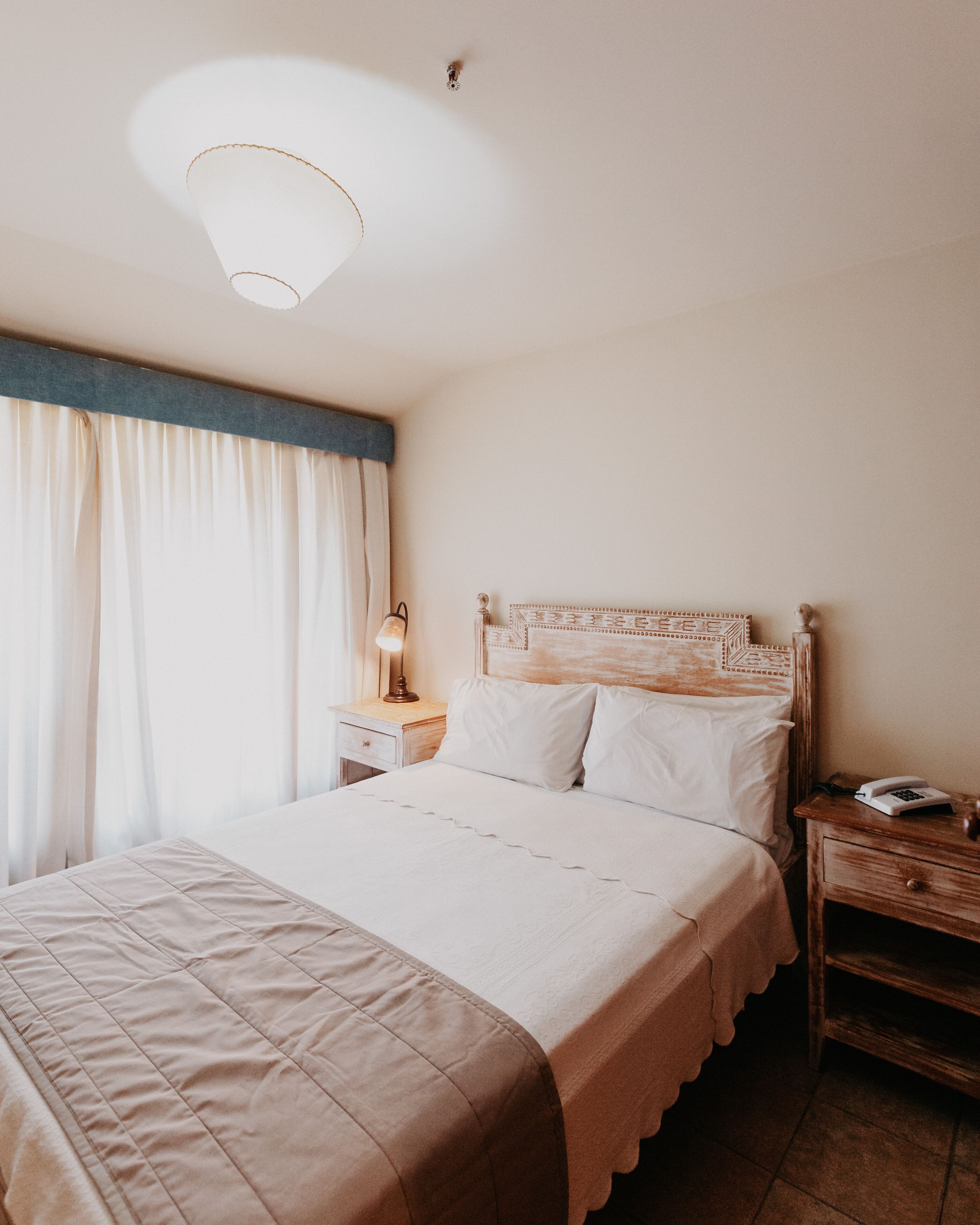 Ein ordentlich bezogenes Bett mit einer gesteppten Decke, einer Nachttischlampe und einem Nachttisch aus Holz mit einem Telefon.