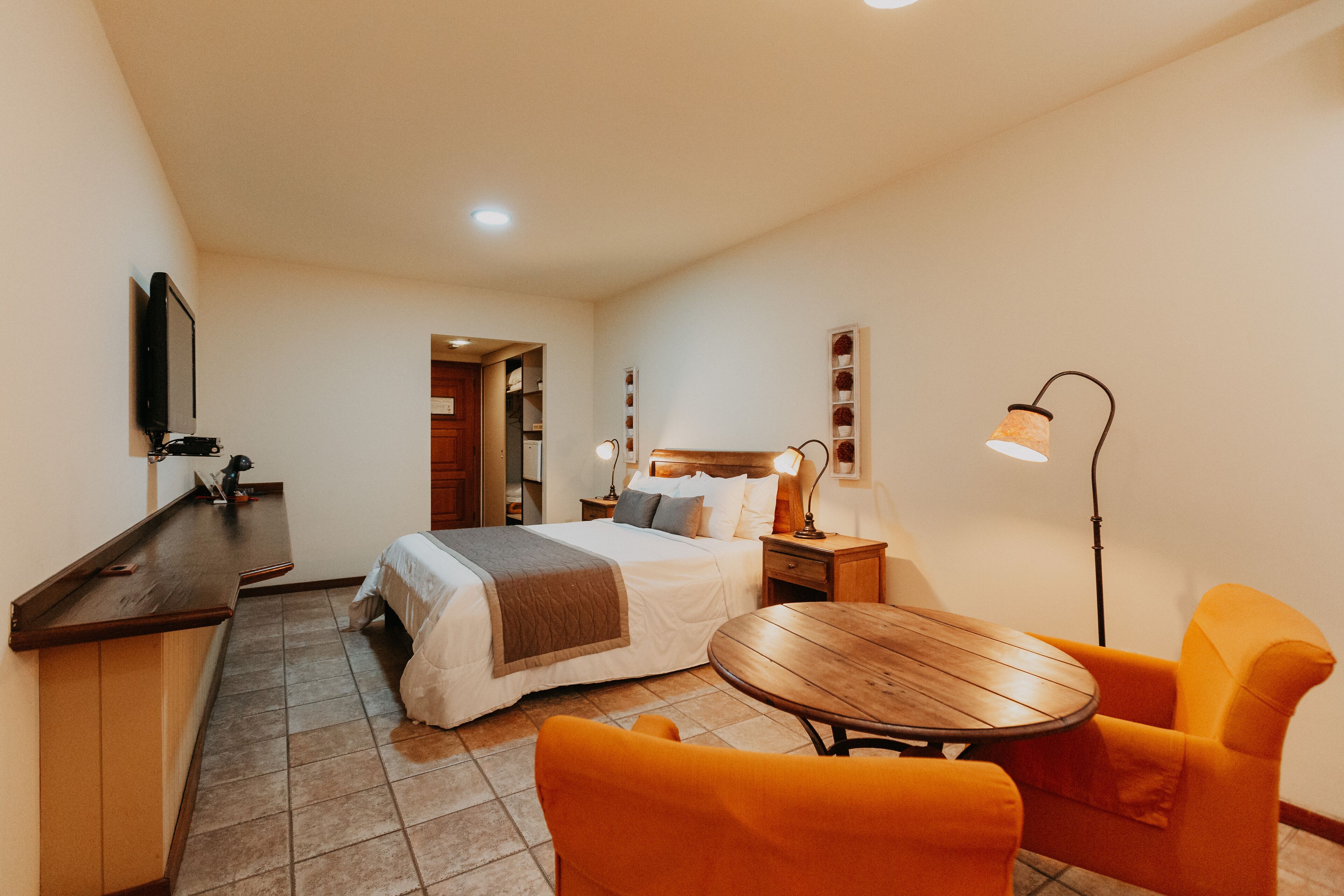 A hotel room with a bed, a desk, a chair, a table, and a lamp.