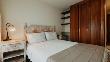 Un dormitorio con cabecera de madera, mesita de noche con lámpara, armario y cama con ropa blanca.