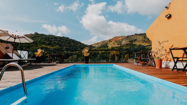 A swimming pool with a wooden deck, surrounded by potted plants and outdoor furniture. - Kastel Itaipava Centro Hotel (Petrópolis)
