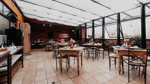 A restaurant with multiple tables and chairs, a large glass enclosure, and a view of the outdoors. - Kastel Itaipava Centro Hotel (Petrópolis)