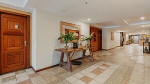 A hotel lobby with a wooden reception desk, tiled flooring, and a large mirror on the wall. - Kastel Itaipava Centro Hotel (Petrópolis)