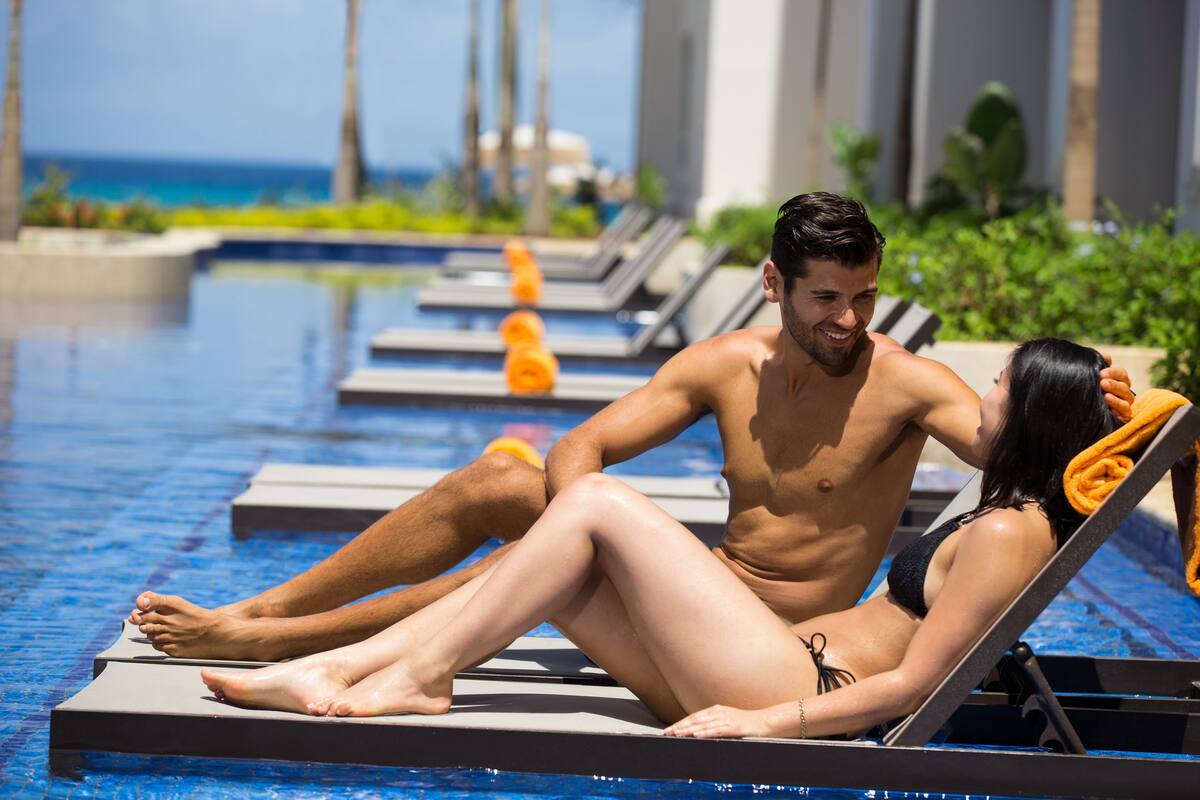 A couple relaxing by a poolside lounge chair with a view of the ocean.