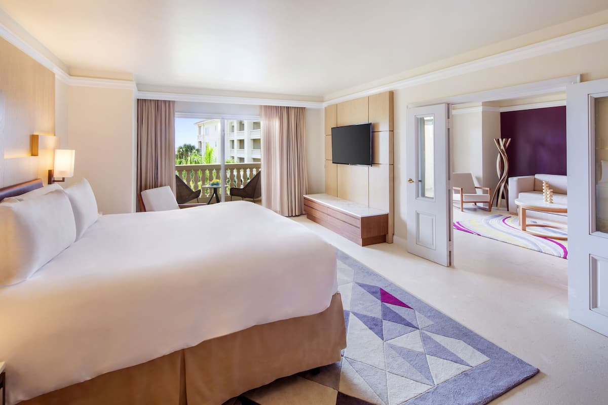 A hotel room with a large bed, a TV mounted on the wall, a balcony with a view, and a desk with a chair.