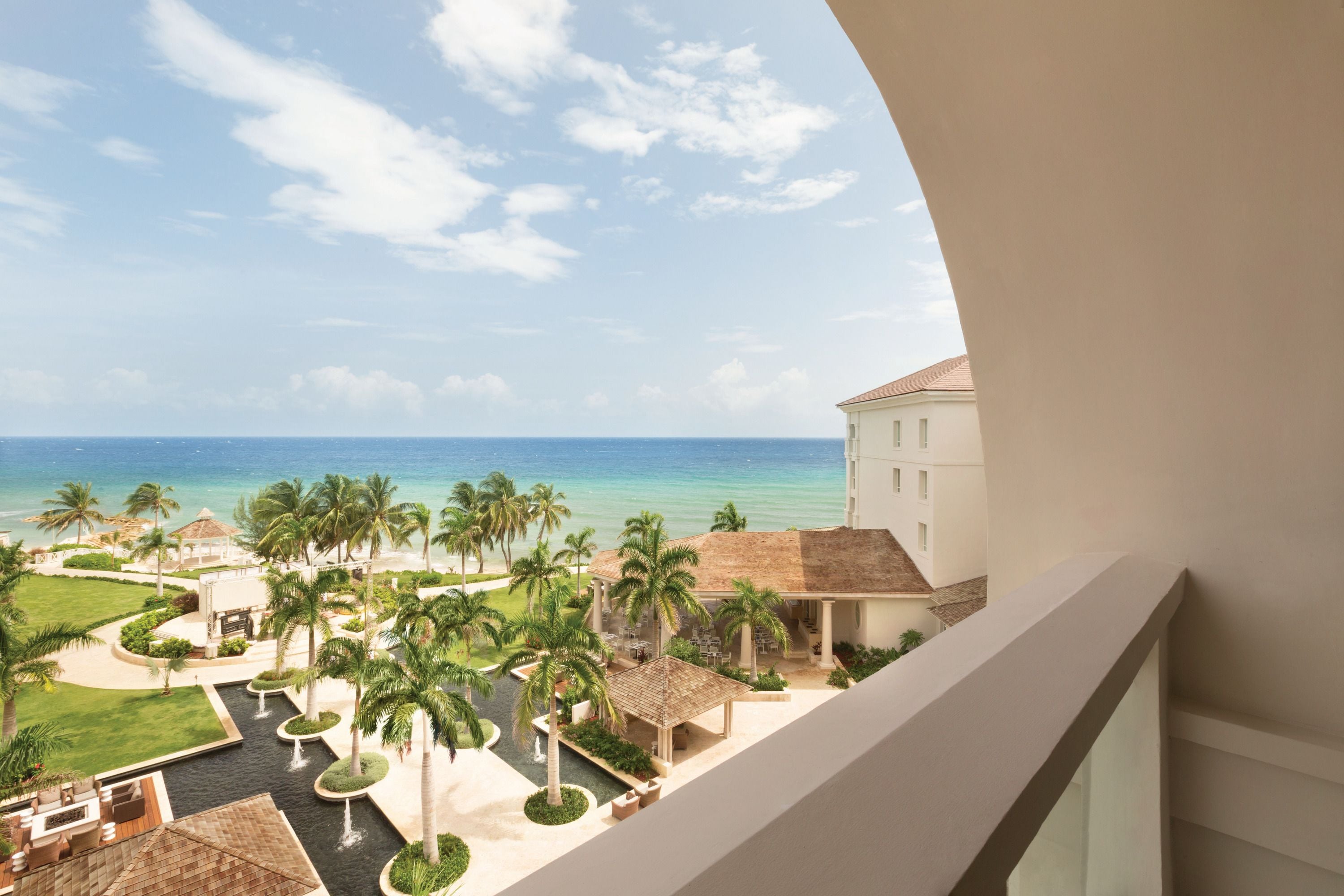 A resort with a pool, palm trees, and a view of the ocean.