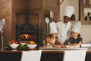 A kitchen with a wood-burning stove, a chef, and two children.