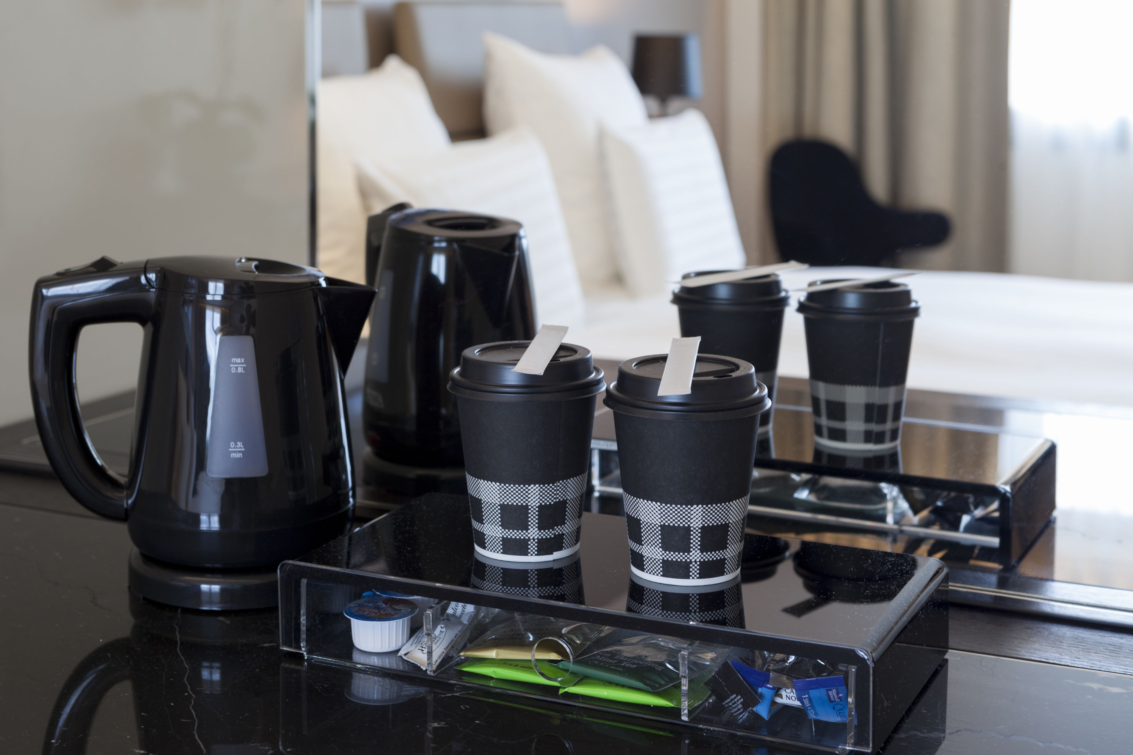 A hotel room with a bed, a coffee maker, and four coffee cups on a tray.