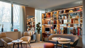 A modern living room with a sofa, two armchairs, a coffee table, and a bookshelf filled with books and decorative items. - AC Porte Maillot Hotel (Paris)