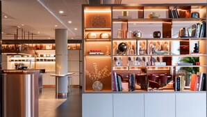 Un intérieur moderne avec une bibliothèque blanche centrale où sont exposés des livres, des objets décoratifs et un globe terrestre.