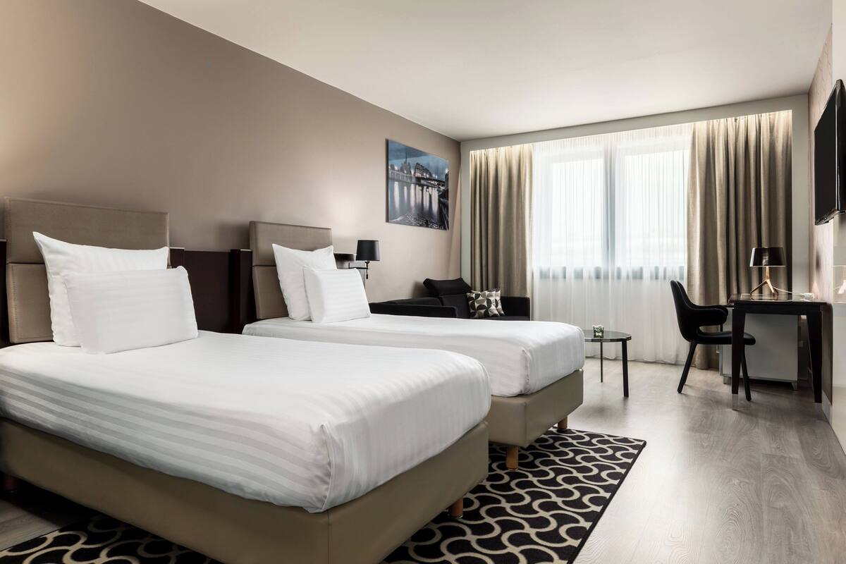 Ein Hotelzimmer mit zwei Betten, einem Schreibtisch, einem Stuhl und einem Fernseher.