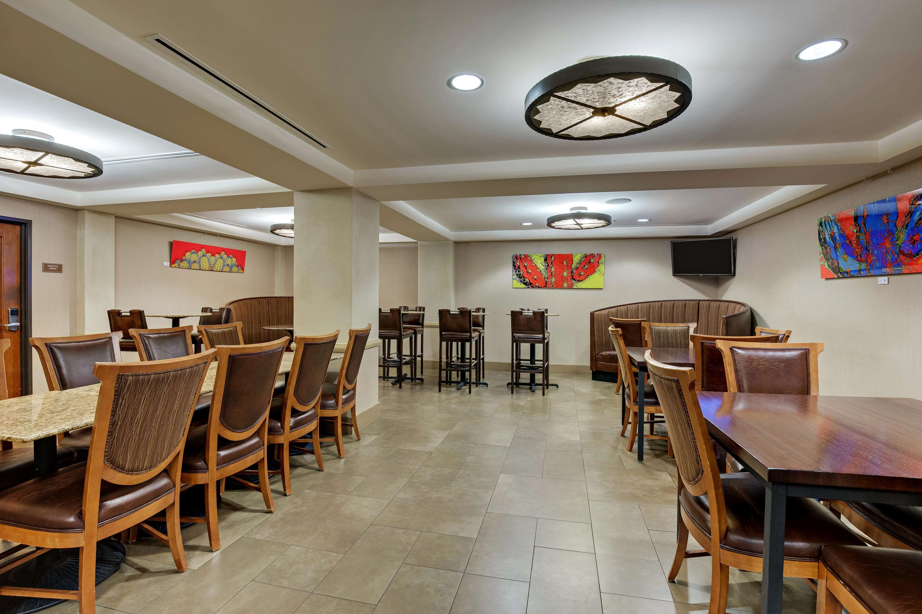 A spacious dining area with multiple tables and chairs, a flat-screen TV mounted on the wall, and ceiling lights.