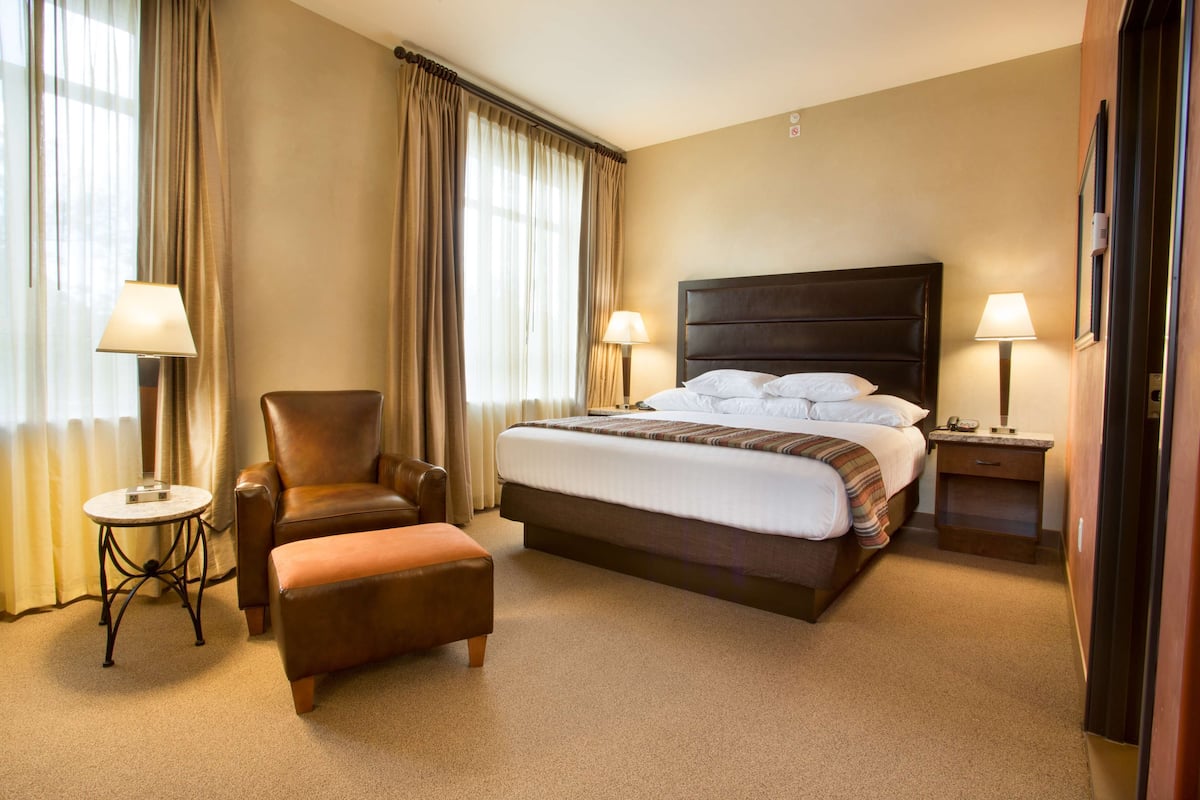 Une chambre d’hôtel avec un grand lit, une chaise, une petite table et une table de chevet avec une lampe.
