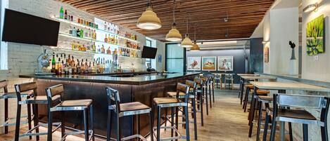 Zona de bar moderna con techo de madera, taburetes y estantes llenos de botellas de licor.