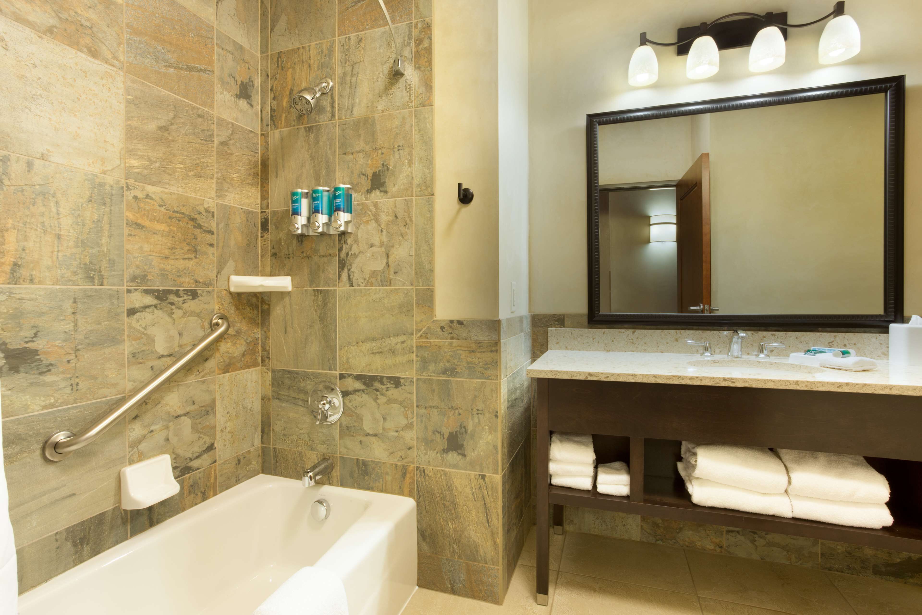 A bathroom with a bathtub, a vanity with a mirror, and toiletries on the wall.