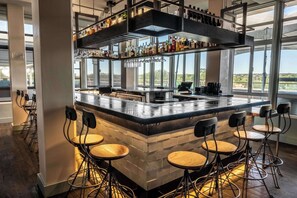 Een bar met een hoge toonbank, krukken en diverse flessen en glazen.