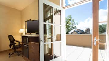 Habitación de hotel con escritorio, silla, televisor y puerta corrediza de vidrio que da a un balcón.
