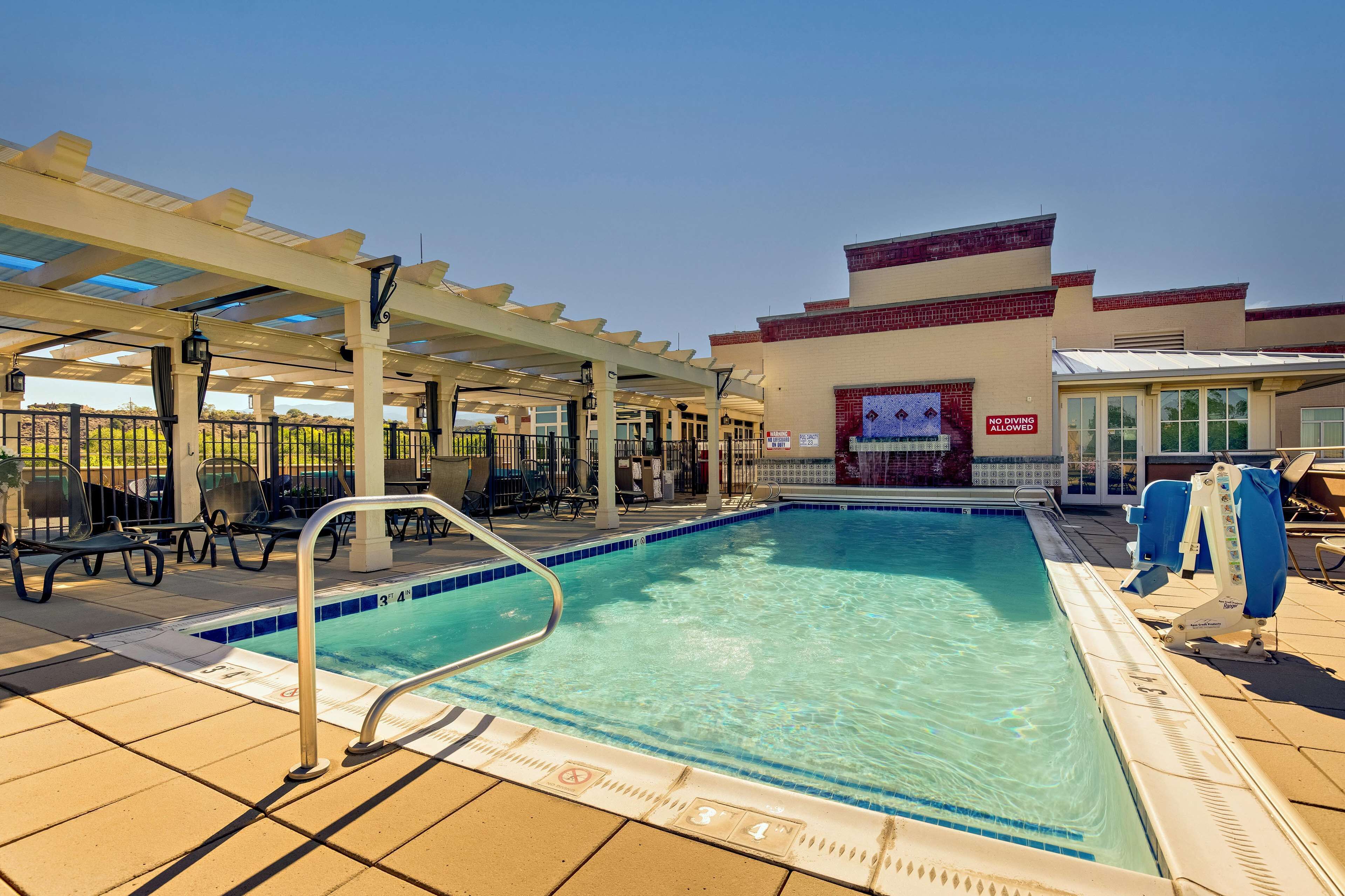 A pool area with a covered seating area, a pool with clear blue water, and a building with a 'No Diving Allowed' sign.