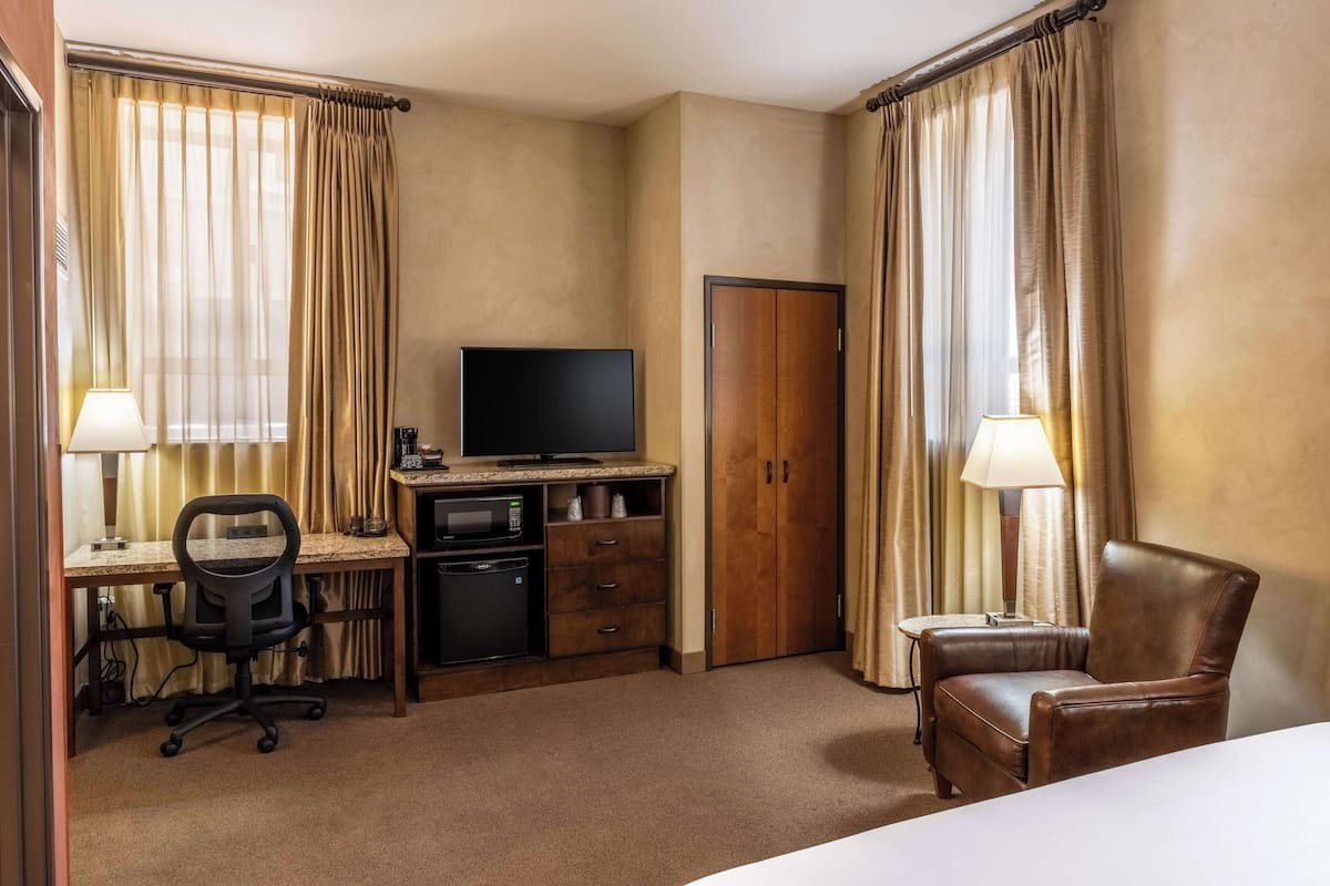 Une chambre d’hôtel comprenant un lit, un bureau avec un ordinateur, une chaise, une télévision, une armoire et une lampe.