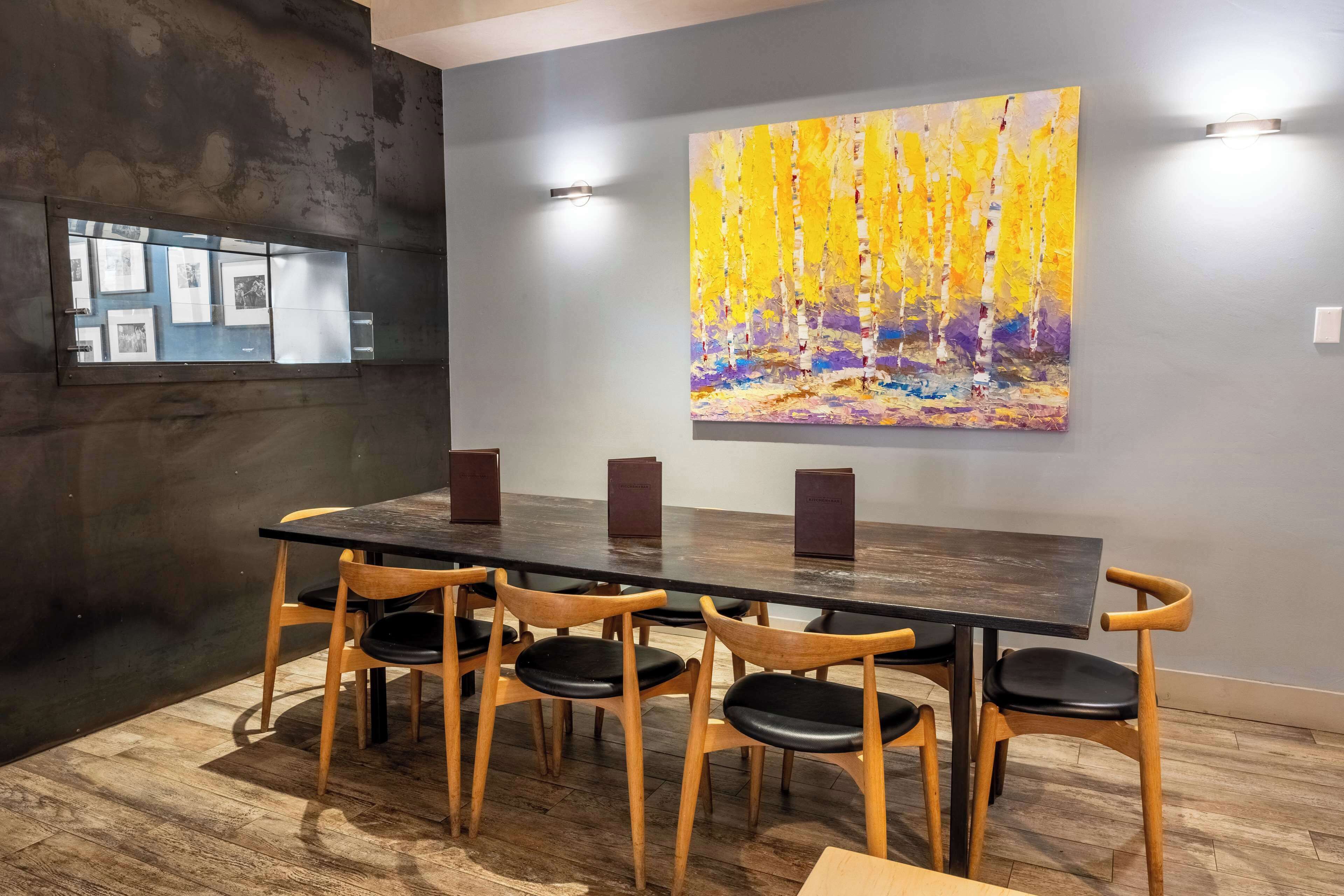 A conference room with a long table, six wooden chairs, and a large abstract painting on the wall.