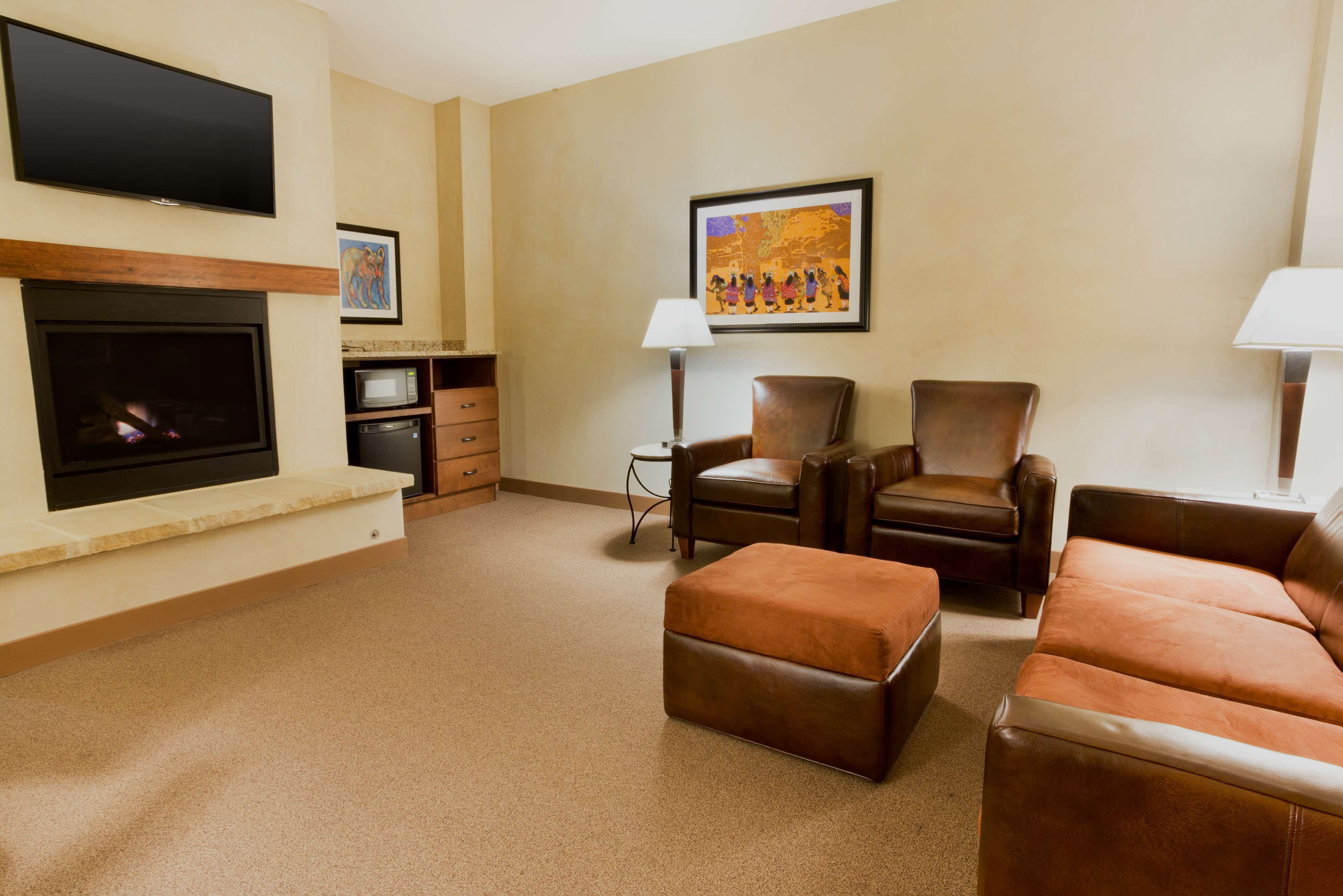 A living room with a flat-screen TV, fireplace, leather sofas, and a framed painting on the wall.