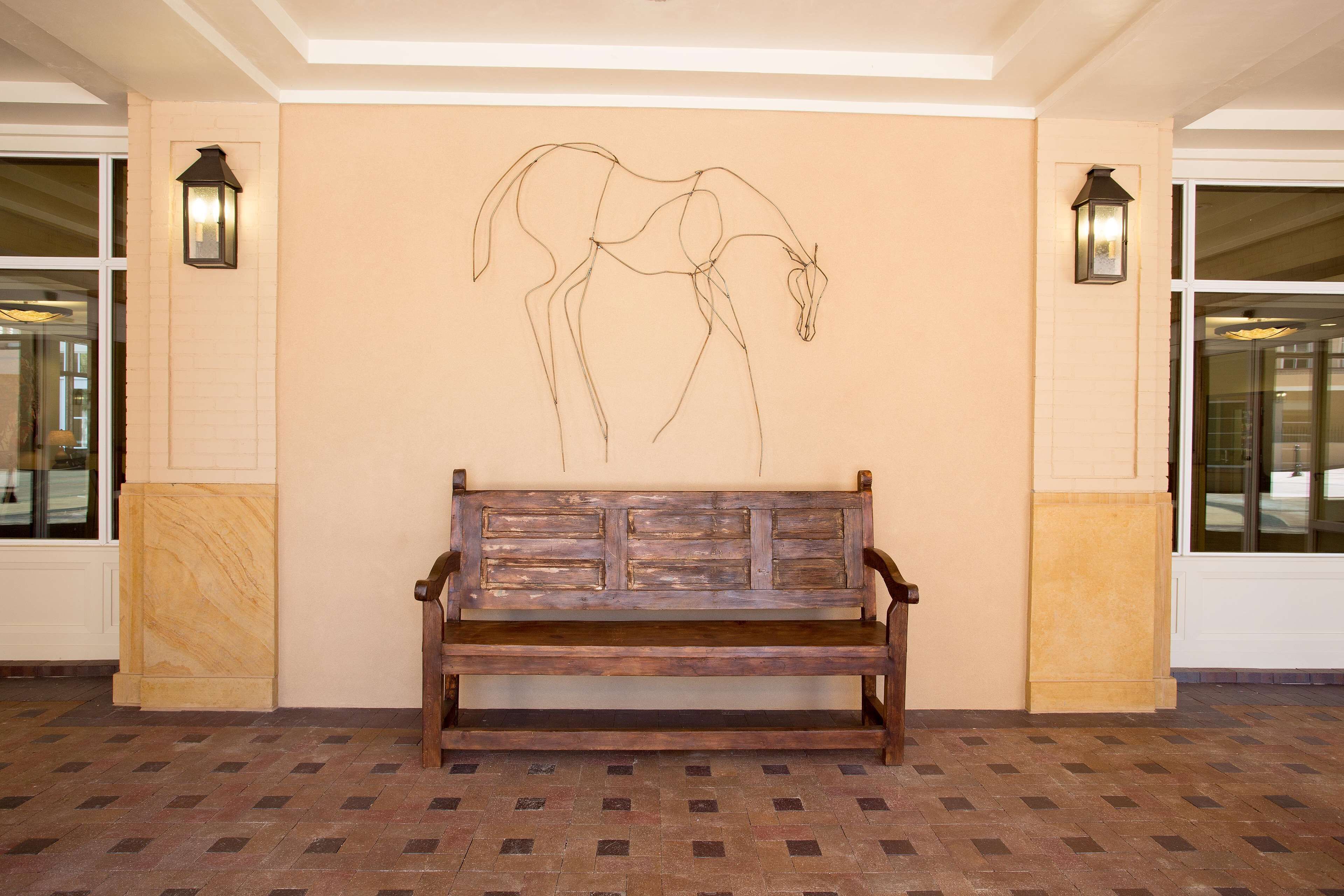 Un banco de madera en un vestíbulo con un dibujo lineal de un caballo colgado en la pared.