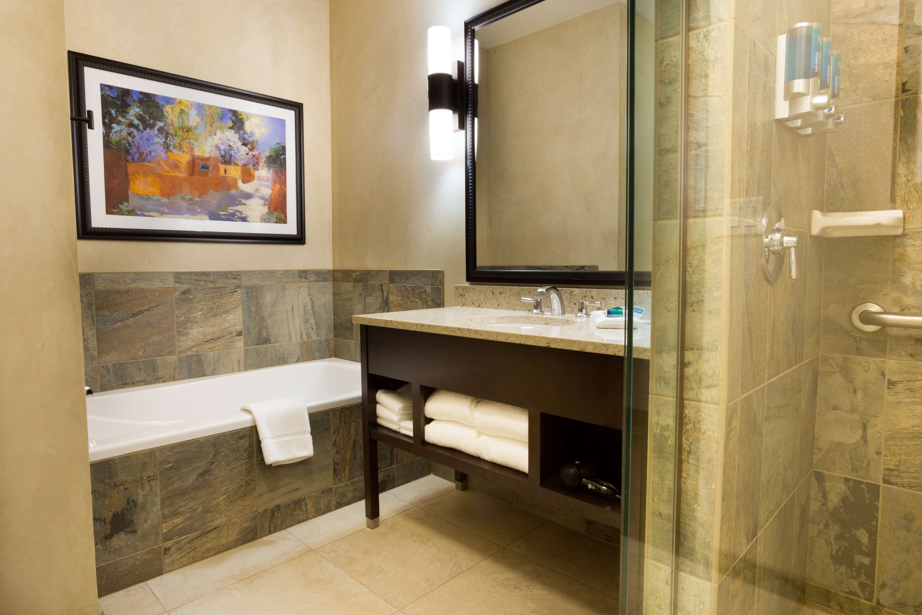 A bathroom with a bathtub, a sink, a mirror, and a framed painting on the wall.