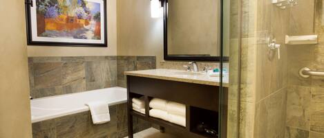 A bathroom with a bathtub, a sink, a mirror, and a framed painting on the wall.