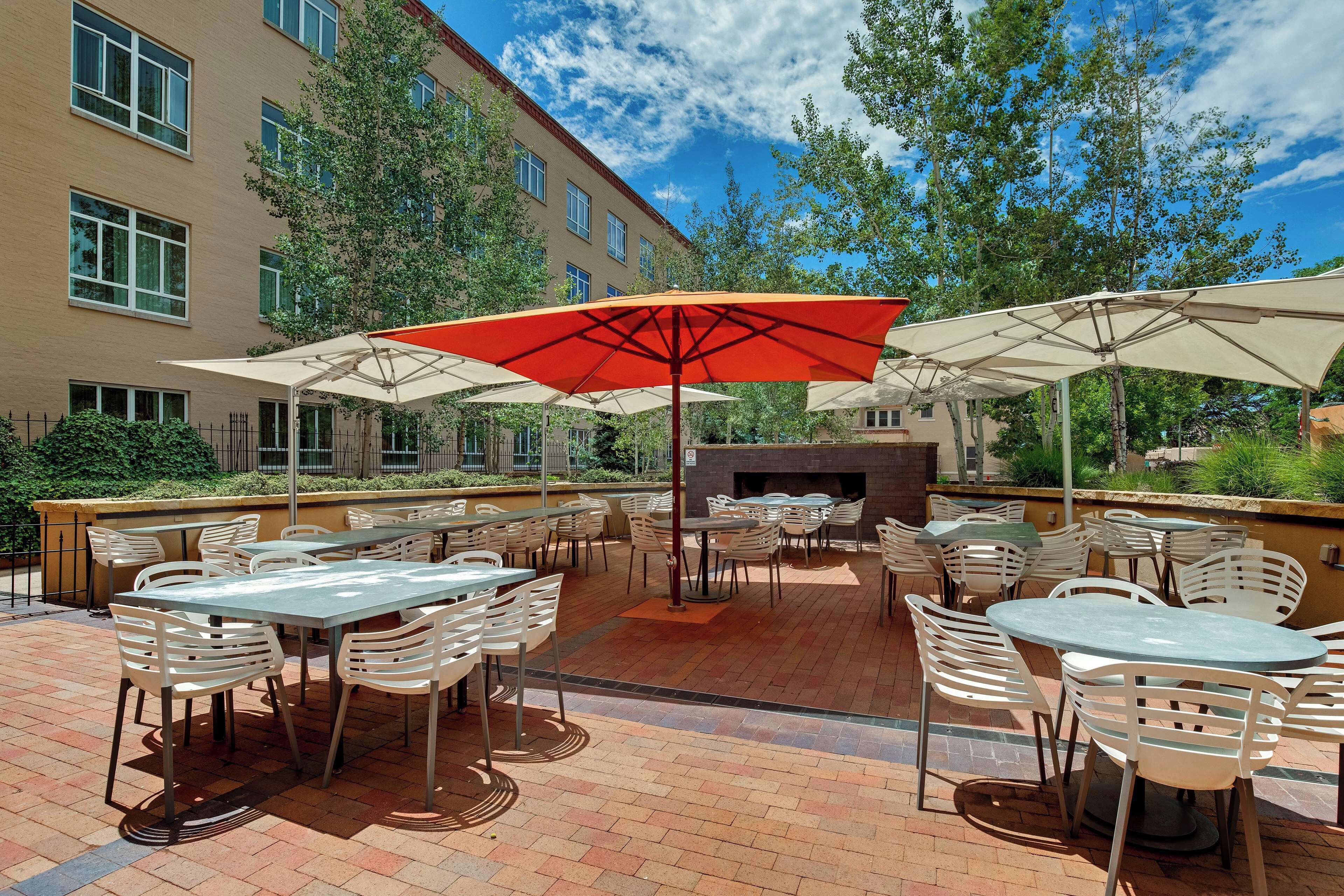An outdoor patio with tables and chairs, a fireplace, and a building in the background.