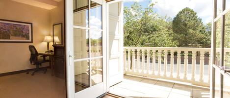 Une porte-fenêtre coulissante donne sur un balcon agrémenté d’une balustrade blanche. On y trouve un bureau avec une chaise, ainsi qu’un tableau encadré accroché au mur.