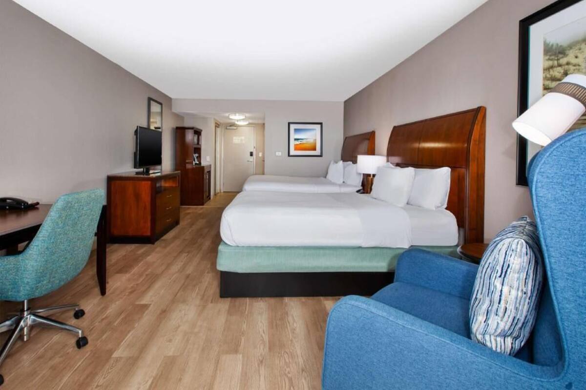 A hotel room with a bed, desk, chair, TV, and a painting on the wall.