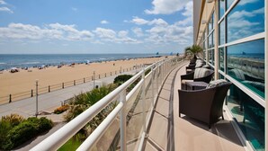 Un balcon doté de meubles en osier, donnant sur une plage sous un ciel dégagé.