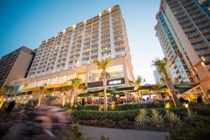 A multi-story hotel with balconies, outdoor seating, and palm trees. - Hilton Garden Inn Virginia Beach Oceanfront (Virginia Beach)