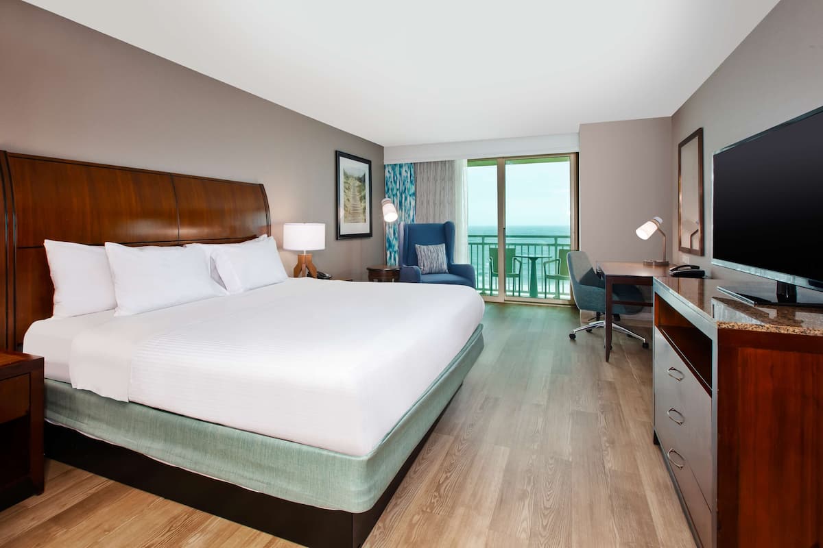 A hotel room with a large bed, a desk with a computer, a chair, and a TV.