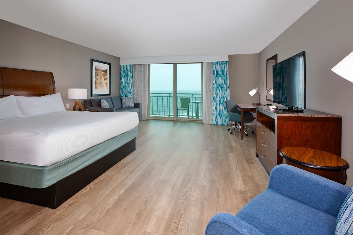 A hotel room with a bed, a desk, a chair, a TV, and a balcony with a view.