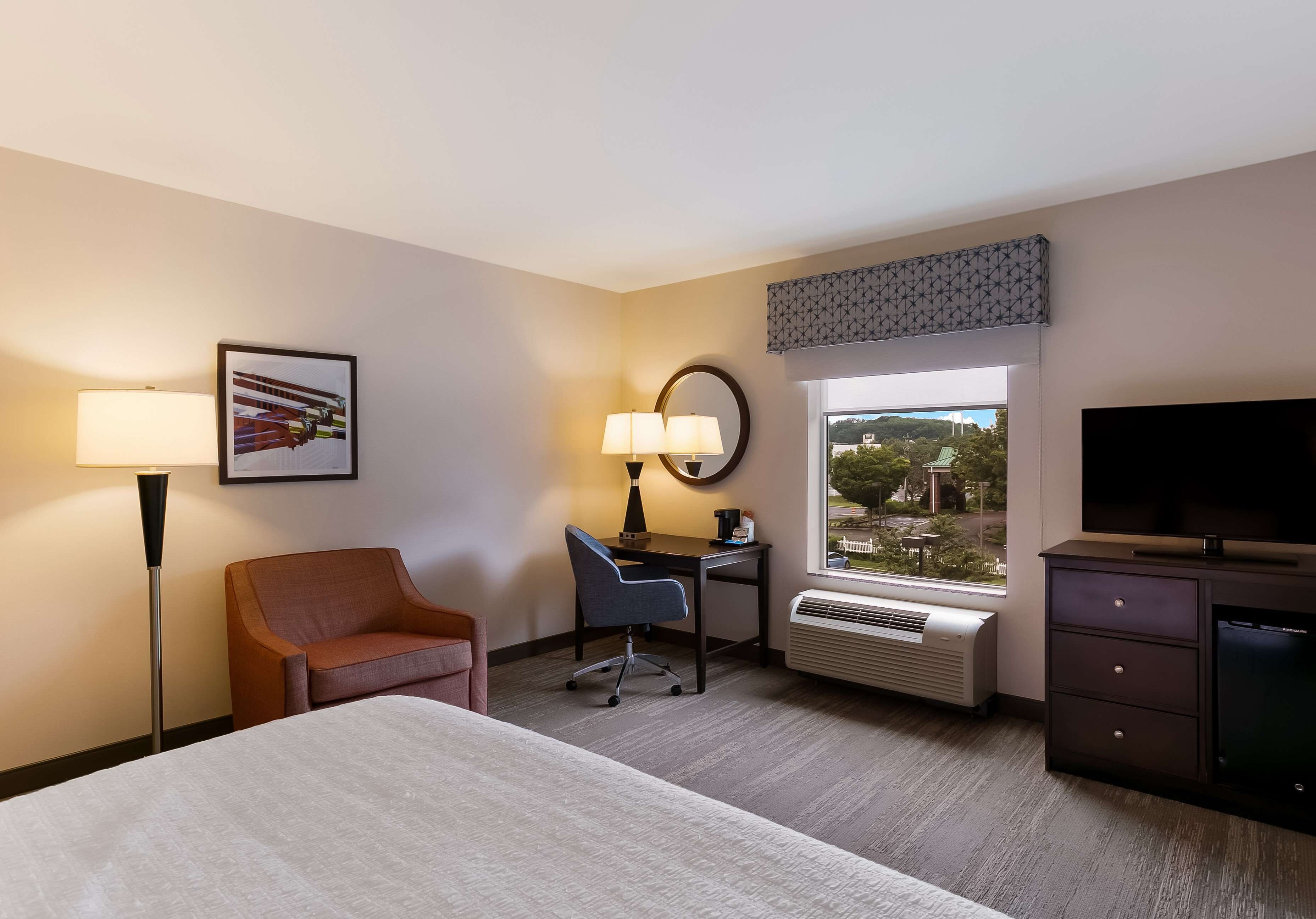 A hotel room with a bed, desk, chair, TV, and a window with a view.