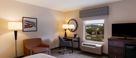 A hotel room with a bed, desk, chair, TV, and a window with a view.