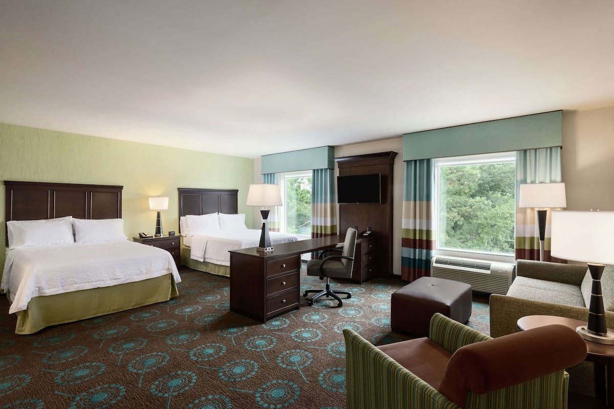 A hotel room with two beds, a desk, a chair, a sofa, and a TV.